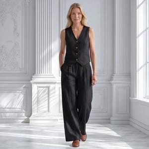 May include: A black sleeveless waistcoat with a V-neckline and four front buttons paired with matching high-waisted wide-leg trousers. The ensemble features a consistent dark fabric texture and is worn with brown leather loafers.