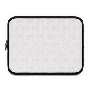 May include: A rectangular laptop sleeve with a white background and a repeating pattern of light pink bows. The sleeve has a black border and a black zipper closure.