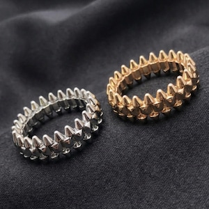 May include: Two circular rings featuring a double row of pointed spikes. One ring is finished in a polished silver tone, while the other ring is finished in a polished gold tone. Both bands have a uniform, repeating spiked texture throughout.