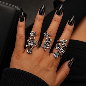May include: A set of four silver-toned rings featuring intricate floral and vine motifs. The rings display detailed petals, leaves, and stems with an oxidized finish, covering multiple fingers with botanical designs including blossoms and rosebuds.