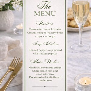 May include: A menu card with a green border and elegant script. The menu lists starters, soup, and main dishes, including quiche Lorraine, roasted pepper soup, and grilled salmon. A champagne flute and gold cutlery are in the background.