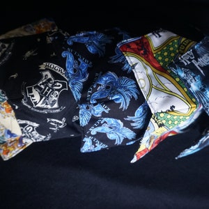 May include: A collection of fabric headbands with various patterns. The headbands feature designs with the Hogwarts crest, blue phoenixes, and other imagery from the Harry Potter series. The colors include black, blue, cream, and red.