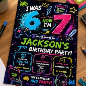May include: A black birthday party invitation card featuring neon-colored video game graphics, including a controller, sword, and headset. The text reads: I WAS 6 NOW I'M 7, JACKSON'S 7TH BIRTHDAY PARTY, SATURDAY AUG 24 2025, GAME ZONE HQ, AND RSVP TO MOM.