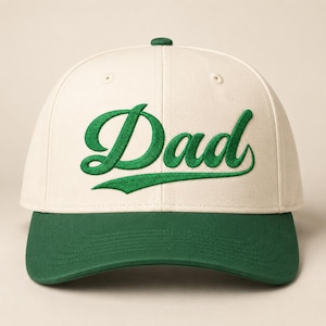 Könnte beinhalten: Baseballkappe mit cremefarbener Krone und grünem Schirm. Das Wort "Dad" ist in grüner Schrift auf die Vorderseite gestickt. Die Kappe hat einen gebogenen Schirm und einen Knopf oben.