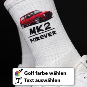 Könnte beinhalten: Weiße Socken mit einer roten Autografik und dem Text "MK2 FOREVER" in Schwarz. Die Socken sind gerippt und scheinen aus einem weichen Material zu sein. Ein weißer Schuh mit schwarzem Streifen ist ebenfalls zu sehen.