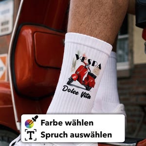 Könnte beinhalten: Weiße gerippte Crew-Socken mit einem Grafikdruck eines roten Rollers, dem Schriftzug VESPA und Dolce Vita sowie einem dezenten grün-weiß-roten Pinselstrich-Design hinter der Roller-Illustration.