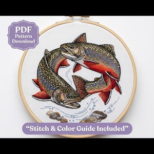 May include: An embroidery hoop containing a fabric piece with two stitched trout fish in shades of brown, orange, and blue. The design includes water ripples and stones. A purple badge reads PDF Pattern Download and Stitch & Color Guide Included.