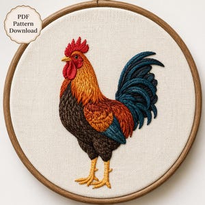 May include: A rooster embroidery design in a circular wooden hoop on cream fabric. The rooster features a red comb, orange and brown neck feathers, a dark brown body, and a blue-black tail. Text in the top left corner reads PDF Pattern Download.