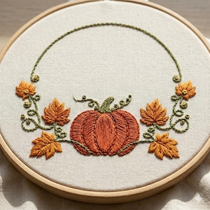 May include: Embroidered artwork showing an orange pumpkin with green vines and leaves, set in a wooden hoop. The design uses autumnal colours. The embroidery is set in a wooden hoop, perfect for autumn decor.