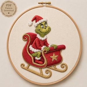 Op de afbeelding: Een ronde houten borduurring met een stoffen paneel met een geborduurd ontwerp van een groen wezen in een rood kerstmanpak in een rode slee met gouden rand en een gouden ster. Een badge in de hoek vermeldt PDF Pattern Download.