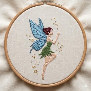 May include: Embroidered fairy artwork in a wooden hoop. The fairy has blue wings, a green dress, and red hair. The embroidery is set in a wooden hoop. The fairy is surrounded by small gold and silver beads.