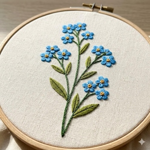 May include: Embroidered forget-me-not flowers in a wooden hoop. The blue flowers have yellow centers and green stems and leaves. The embroidery is on a cream-colored fabric.
