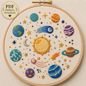 Puede incluir: Un bastidor de bordado que contiene un panel de tela con un diseño de sistema solar cosido a mano. La pieza presenta un sol amarillo central rodeado de varios planetas, estrellas, una luna creciente y cometas en hilos azules, naranjas y morados.