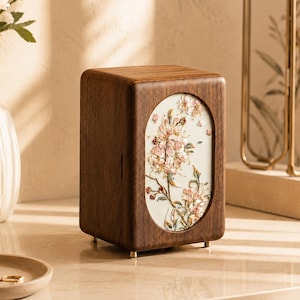 May include: A rectangular dark brown wooden storage box featuring a vertical oval inlay on the front panel. The inlay displays a raised, textured floral design in shades of pink, white, and green against a cream-coloured background.