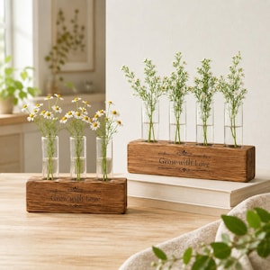 May include: Two rectangular wooden blocks with glass test tube vases. The front of each block features the engraved text "Grow with Love" with decorative flourishes. Each glass tube contains small white flowers with green stems and leaves.