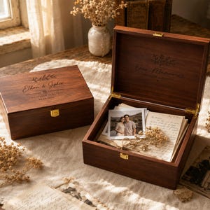 Könnte beinhalten: Zwei rechteckige Aufbewahrungsboxen aus dunklem Holz mit goldenen Verschlüssen. Eine Box ist geschlossen und mit dem Text Ethan & Sophie, Together Always und 05.10.2025 graviert. Die offene Box enthält ein Foto eines Paares, Briefe und Trockenblumen.