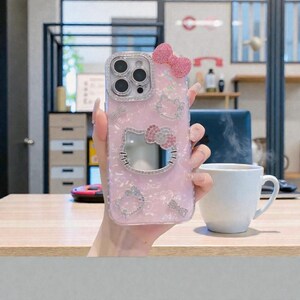 May include: A pink phone case with a Hello Kitty design, featuring a bow and sparkling accents. The case has a clear border and a cut-out for the camera. The design includes multiple Hello Kitty figures and decorative elements.