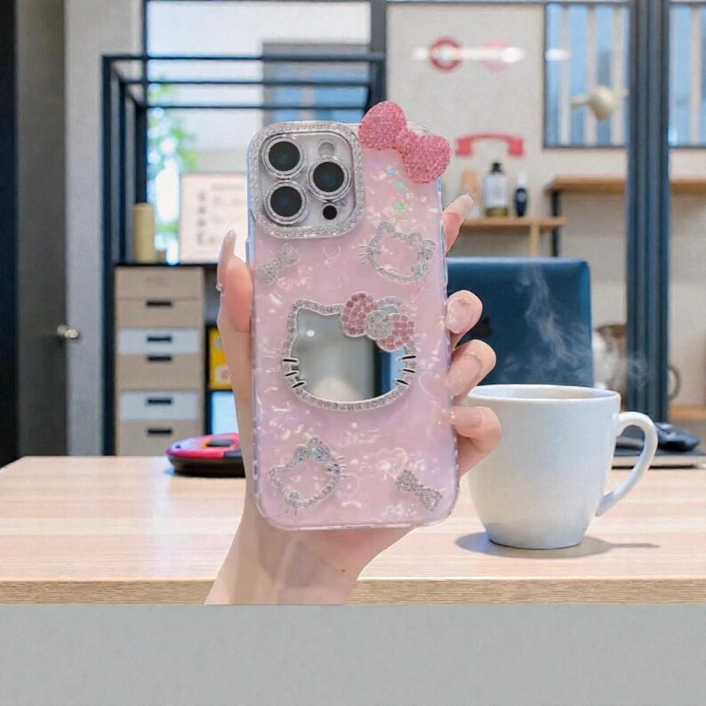 May include: A pink phone case with a Hello Kitty design, featuring a bow and sparkling accents. The case has a clear border and a cut-out for the camera. The design includes multiple Hello Kitty figures and decorative elements.
