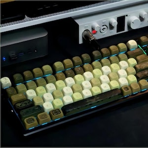 May include: A mechanical keyboard with a unique design. The keycaps are a mix of olive green, cream, and brown, with a vintage aesthetic. The keyboard has a blue underglow and is set up with audio equipment.