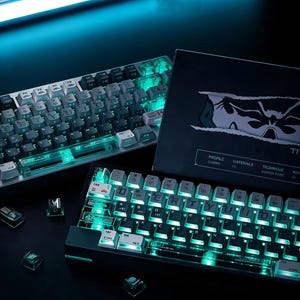 May include: Two illuminated mechanical keyboards with white keycaps and teal backlighting are displayed. The keyboards are next to a black box with a graphic design. Several clear keycaps are scattered around the keyboards, and a bright blue light is above.