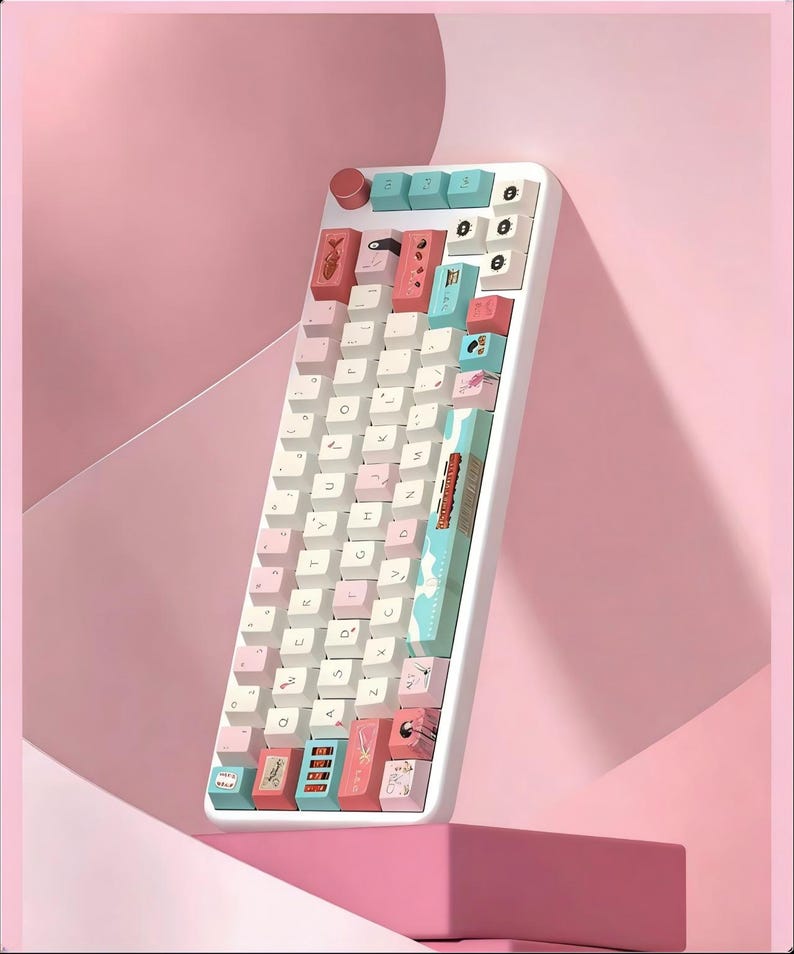 K&ouml;nnte beinhalten: Eine wei&szlig;e mechanische Tastatur mit pastellfarbenen rosa, blauen und wei&szlig;en Tastenkappen. Die Tastatur hat ein einzigartiges Design mit individuellen Tastenkappen mit Illustrationen. Die Tastatur ist abgewinkelt und vor einem rosa Hintergrund platziert.