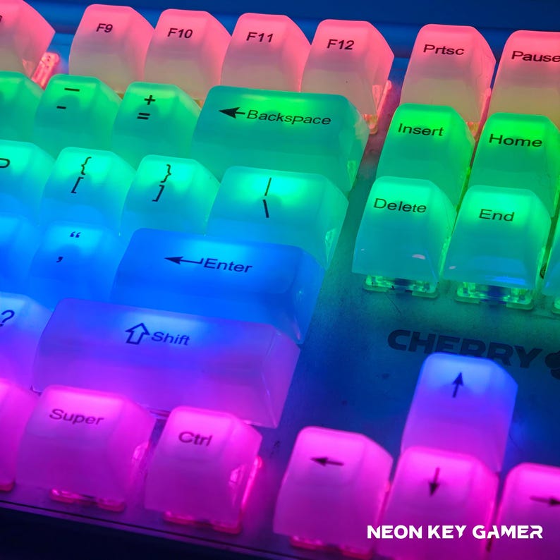 May include: Close-up of a backlit keyboard with transparent keycaps. The keys are illuminated with a gradient of colors, including pink, green, and blue. Key labels such as "Enter", "Shift", and "Backspace" are visible. The text "NEON KEY GAMER" is at the bottom.