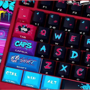 May include: A close-up of a red mechanical keyboard with black keys and graffiti-style lettering. The keys have a mix of blue, pink, and white accents. Key labels include "TAB", "CAPS", "SHIFT", "CTRL", and "WIN".