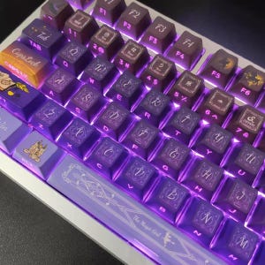 May include: A custom mechanical keyboard with purple and brown keycaps. The keycaps feature various symbols, letters, and designs, with the text "The Magic Girl" on the spacebar. The keyboard has a white frame and purple underglow.
