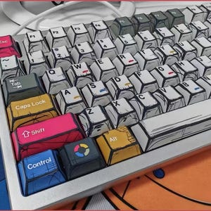 May include: A mechanical keyboard with custom keycaps. The keycaps have a unique comic book style design with black outlines and colorful accents. The keyboard has a silver frame and a variety of function keys, including Esc, Tab, Shift, and Control.
