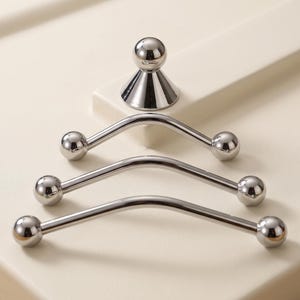 May include: A set of three polished silver-toned curved metal bars with spherical ends, arranged in a descending size order, accompanied by a single small silver-toned conical base with a spherical top, all featuring a smooth, reflective finish.