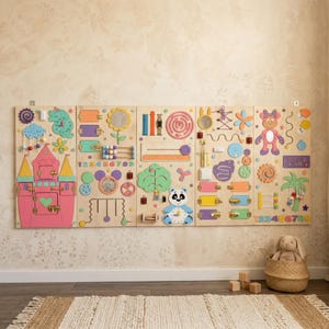 Puede incluir: Un gran tablero de actividades sensoriales de madera con cinco paneles conectados que incluyen varios elementos interactivos como un castillo rosa, un reloj de panda, engranajes, pestillos, espejos, laberintos, cuentas y números.