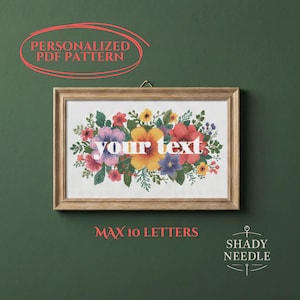 Op de afbeelding: Een ingelijst bloemenkruissteekpatroon met de tekst "your text" in het midden. De bloemen zijn in tinten rood, geel, paars en blauw. De tekst "MAX 10 LETTERS" staat onder het frame. De woorden "PERSONALIZED PDF PATTERN" staan boven het frame.