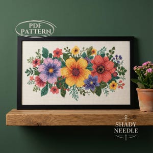 May include: A framed cross-stitch floral pattern featuring a vibrant bouquet of colorful flowers. The design includes blooms in shades of purple, yellow, red, and blue, with green foliage. The words "PDF PATTERN" are in the upper left corner.