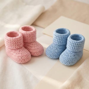 Pu&ograve; includere: Due paia di scarpine fatte a mano per neonati. Un paio &egrave; rosa chiaro, l'altro azzurro. Le scarpine sono lavorate all'uncinetto con un design a risvolto. La consistenza morbida e i colori suggeriscono un articolo per neonati fatto a mano e accogliente.