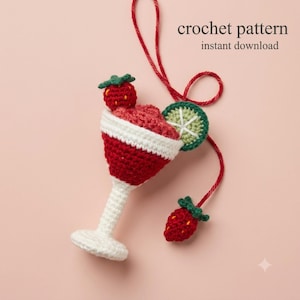Könnte beinhalten: Eine Häkelanleitung als Sofort-Download mit einem gehäkelten Cocktailglas-Ornament in Rot und Weiß. Das Glas ist mit einer roten Erdbeere, einer grünen Limettenscheibe und einer kleinen roten Erdbeere an einer roten Garnschnur verziert.