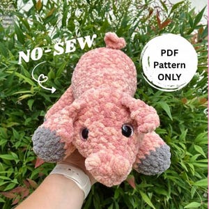 May include: A handmade pink and gray crochet pig with large black eyes. The pig has a textured, plush appearance and the text "NO-SEW" and "PDF Pattern ONLY" are visible.