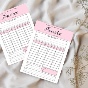May include: Two pink and white invoice pads with the word "Invoice" in elegant script. The pads have sections for customer information and item details. The pads are on a white fabric surface.
