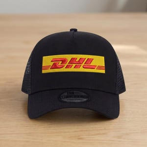 May include: Black trucker hat with the DHL logo in red and yellow. The hat features a mesh back and an adjustable strap. The DHL logo is prominently displayed on the front.