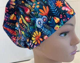 May include: A scrub cap featuring a dark blue background with a vibrant, multi-colored floral and botanical print. The pattern includes various stylized flowers, leaves, and stems in shades of orange, pink, yellow, and light blue, covering the entire fabric surface of the head covering.