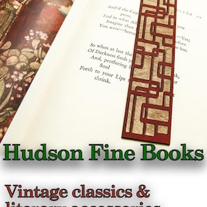 May include: A wooden bookmark with a geometric design in shades of brown and red. The bookmark is on top of an open book with text about the "Cup" and "Darkness". The text below the bookmark reads "Hudson Fine Books Vintage classics & literary accessories for discerning readers..."
