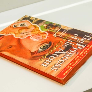 May include: A vintage paperback book titled "The Princess of the Atom" by Ray Cummings. The cover features a woman's eye with a red, orange, and yellow background.