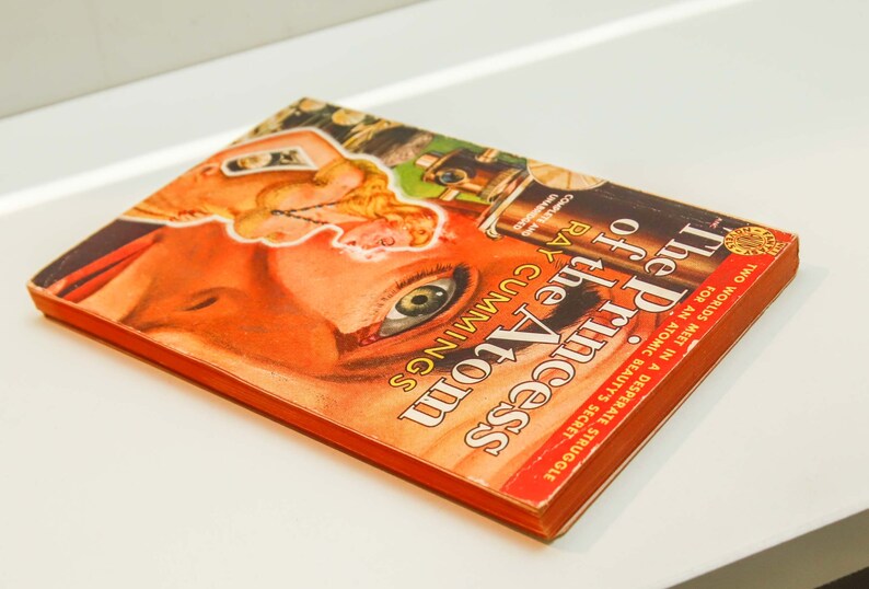 May include: A vintage paperback book titled "The Princess of the Atom" by Ray Cummings. The cover features a woman's eye with a red, orange, and yellow background.