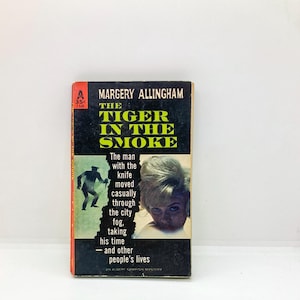 May include: Vintage paperback book titled "The Tiger in the Smoke" by Margery Allingham. The cover features a black background with yellow text, an illustration of a man with a knife, and a woman's portrait. The book is a mystery novel.