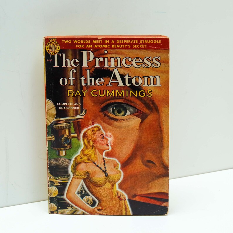 May include: A vintage paperback book cover with a red, white, and blue design. The title is "The Princess of the Atom" by Ray Cummings. The cover features a woman's eye and a woman in a yellow dress.