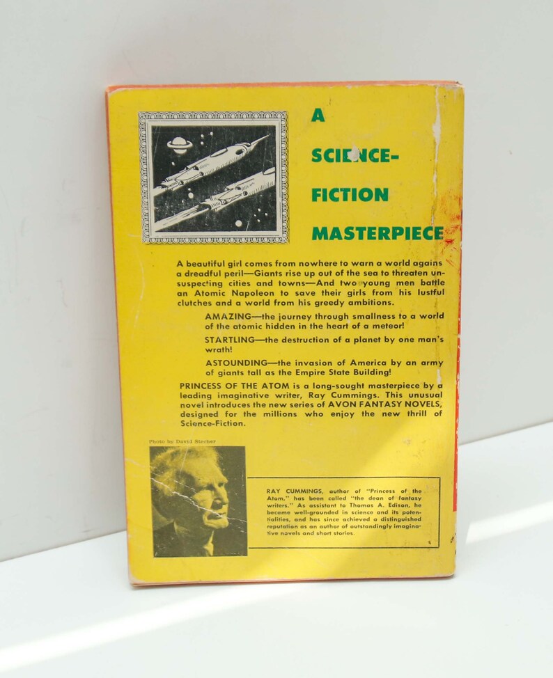 May include: A yellow and black book cover with a science fiction theme. The cover features a black and white illustration of a spaceship and a planet. The title of the book is "Princess of the Atom" and the author is Ray Cummings. The book is part of the Avon Fantasy Novels series.