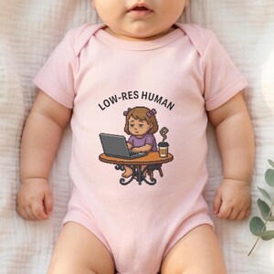 Peut inclure: Body rose clair pour bébé avec l'inscription "LOW-RES HUMAN" et une illustration de dessin animé. L'illustration représente une personne travaillant sur un ordinateur portable à une table, avec une tasse de café.