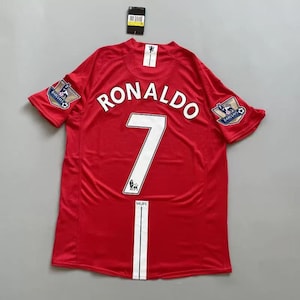 May include: Red soccer jersey with the name "RONALDO" and the number "7" in white. Features the "Barclays" logo on the sleeves and the "MUFC" logo at the bottom. A black tag is attached at the top.