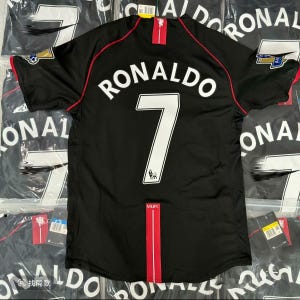 Op de afbeelding: Zwart voetbalshirt met de naam "RONALDO" en het nummer "7" in het wit. Het shirt heeft rode accenten en het MUFC-logo. Het shirt is nieuw.