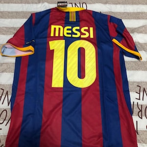 May include: A blue and red striped soccer jersey with the name "MESSI" and the number "10" in yellow. The jersey has a yellow collar and sleeve trim. The jersey is made of a lightweight material.