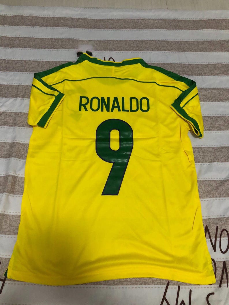 May include: A yellow football shirt with green detailing. The name "RONALDO" is printed on the back in black, with the number "9" below in green. The shirt is made of a lightweight fabric.